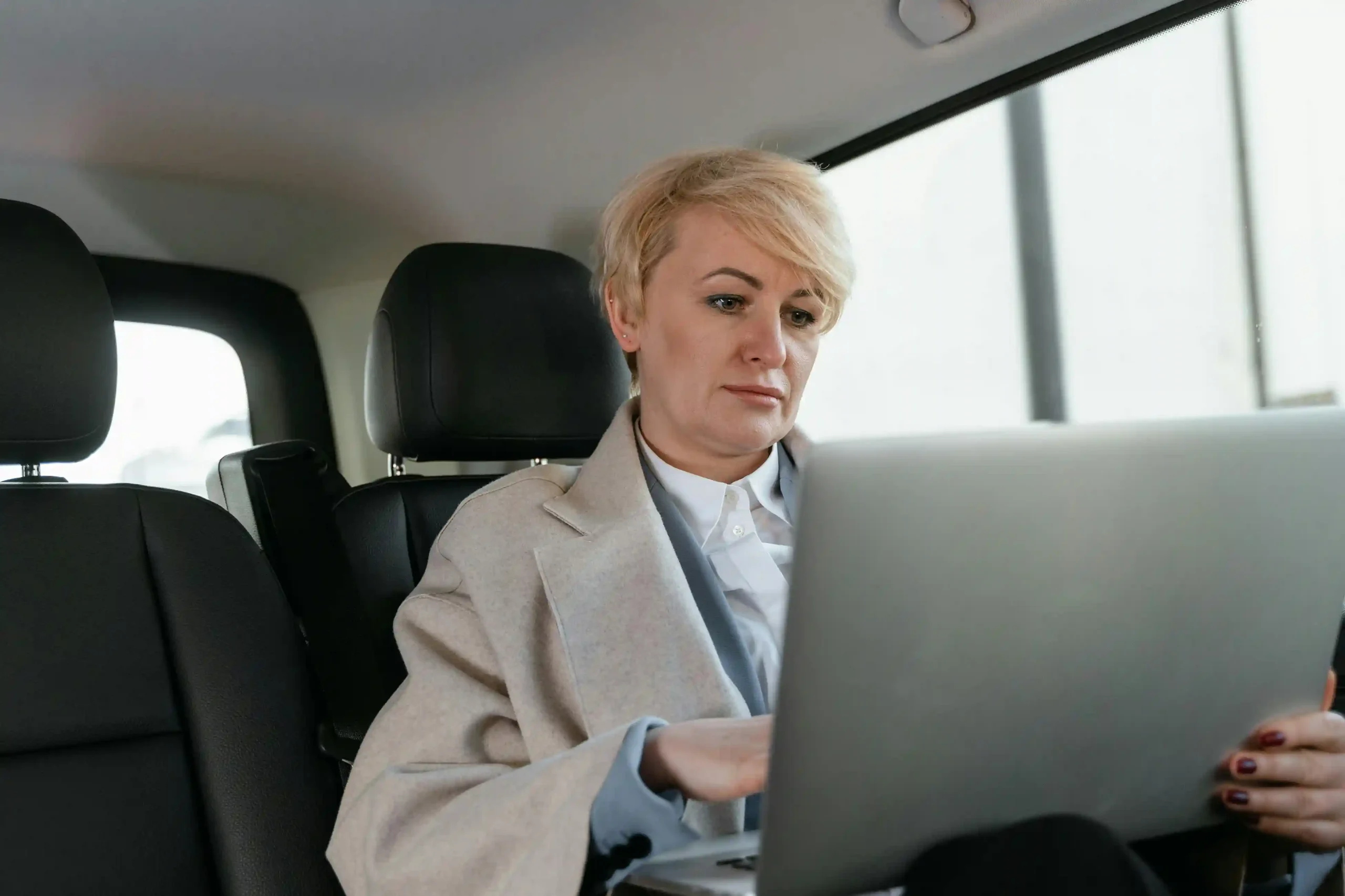 Focused businesswoman working on a laptop in the backseat of a car