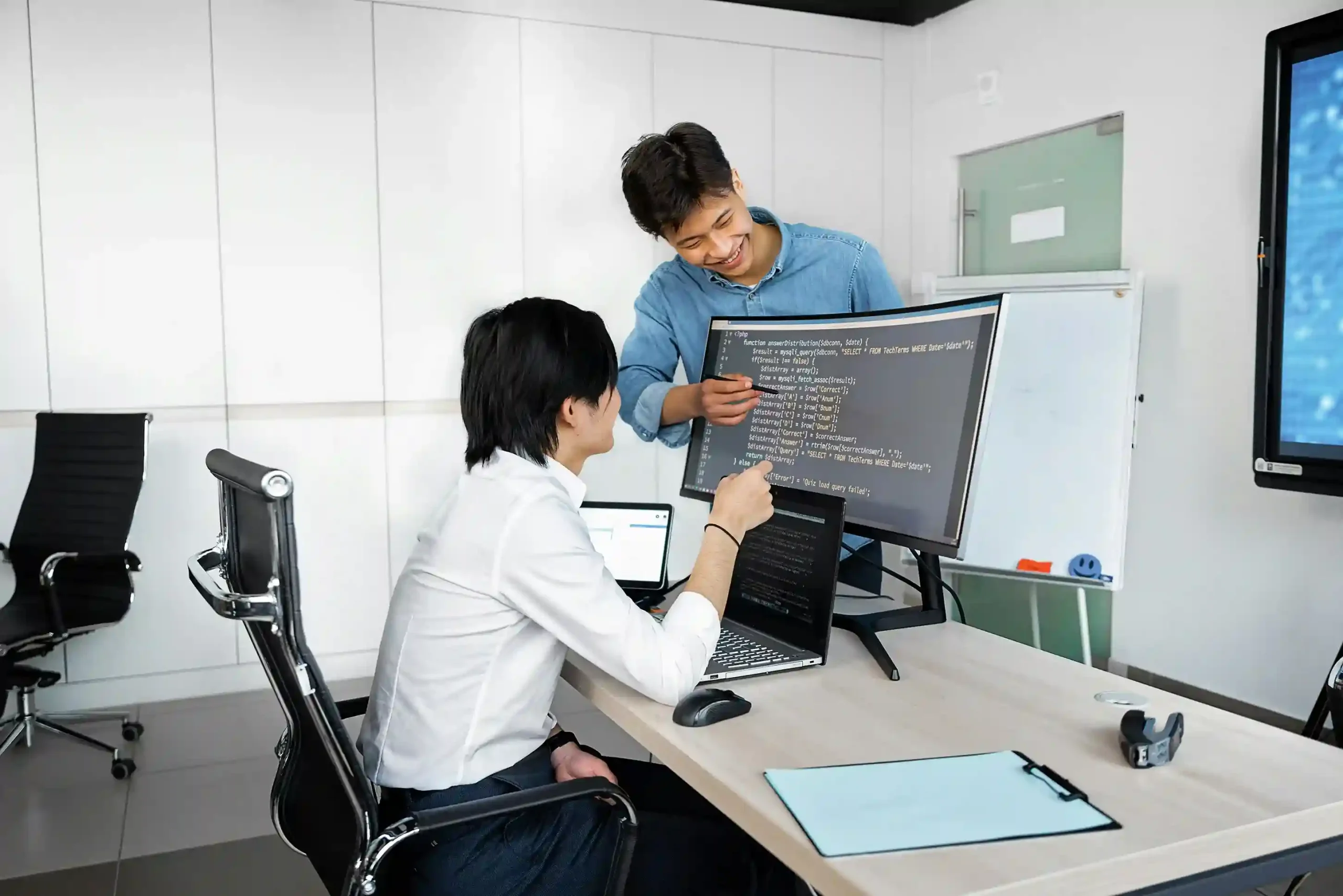 Two software developers collaborating in an office, discussing code displayed on a monitor.
