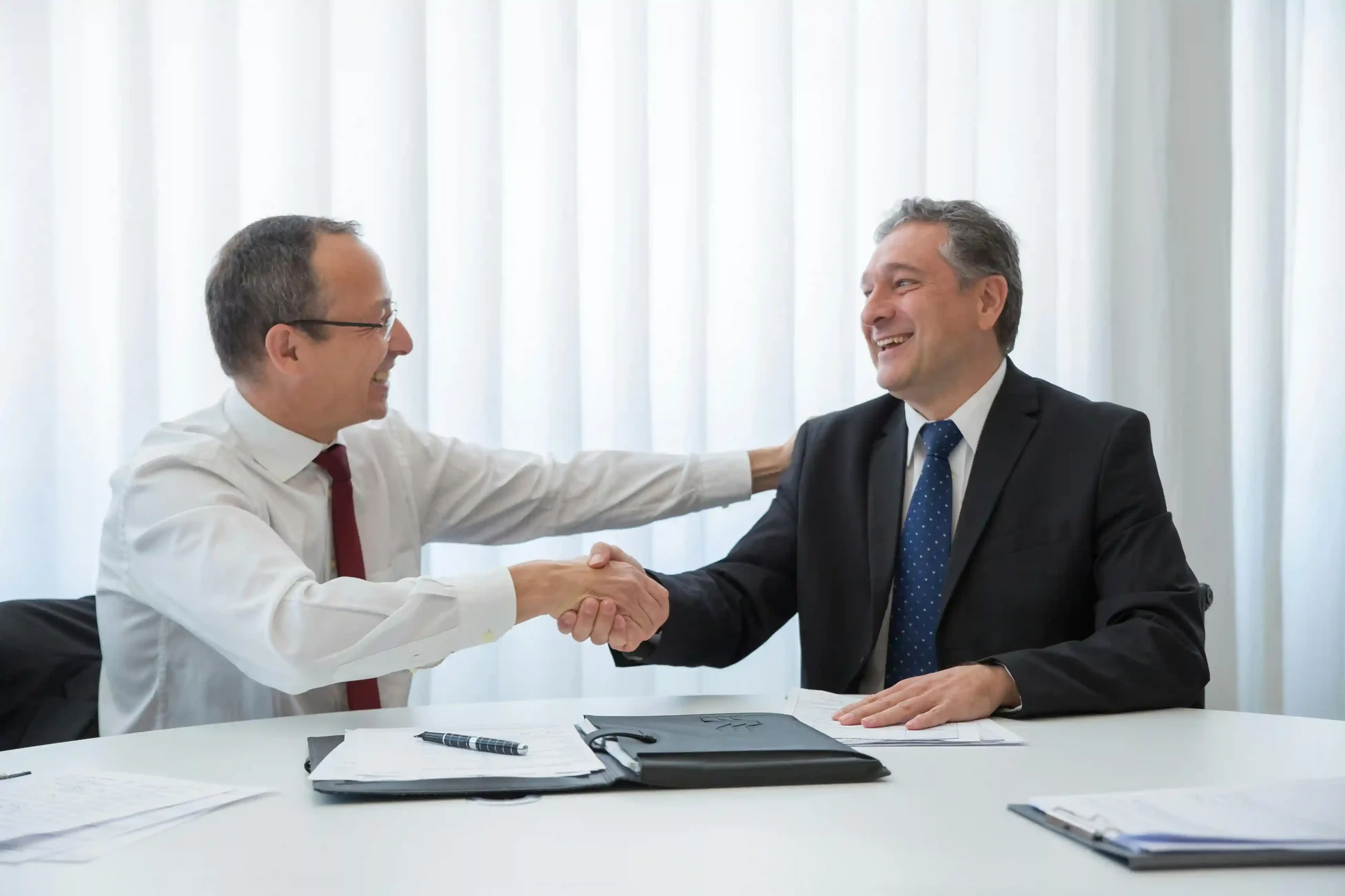 Two businessmen in formal attire shaking hands and smiling during a meeting
