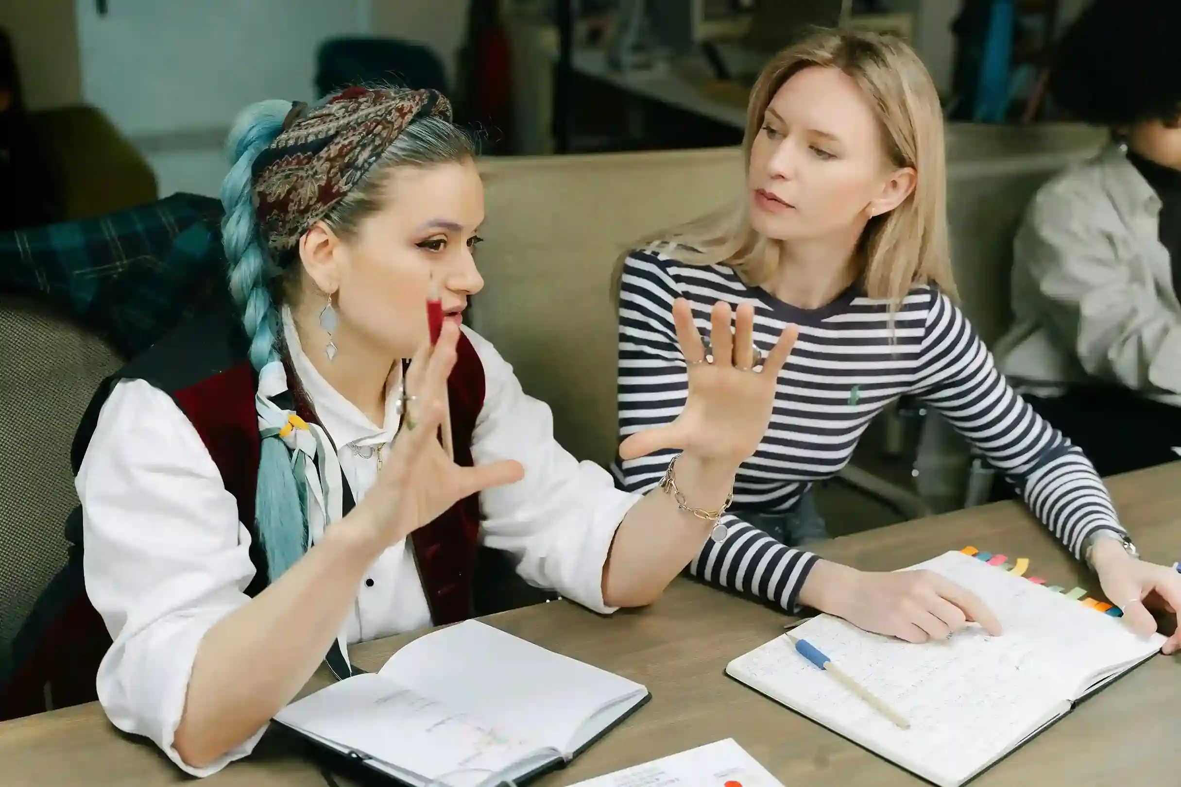 Two women in a discussion at a table with notebooks and pens in an office setting