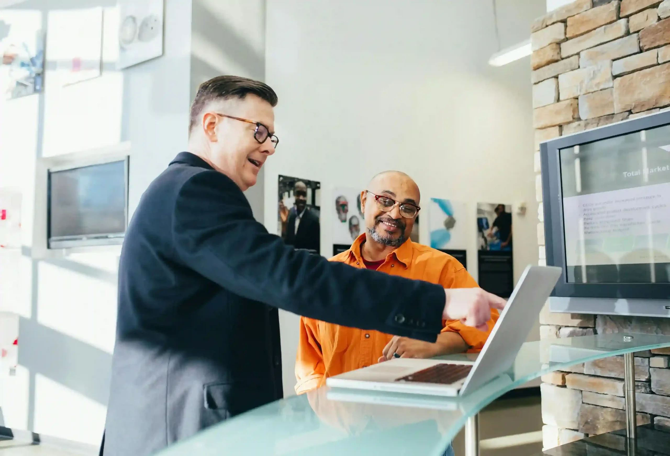 Two businessmen discussing something on a laptop in a modern office setting.