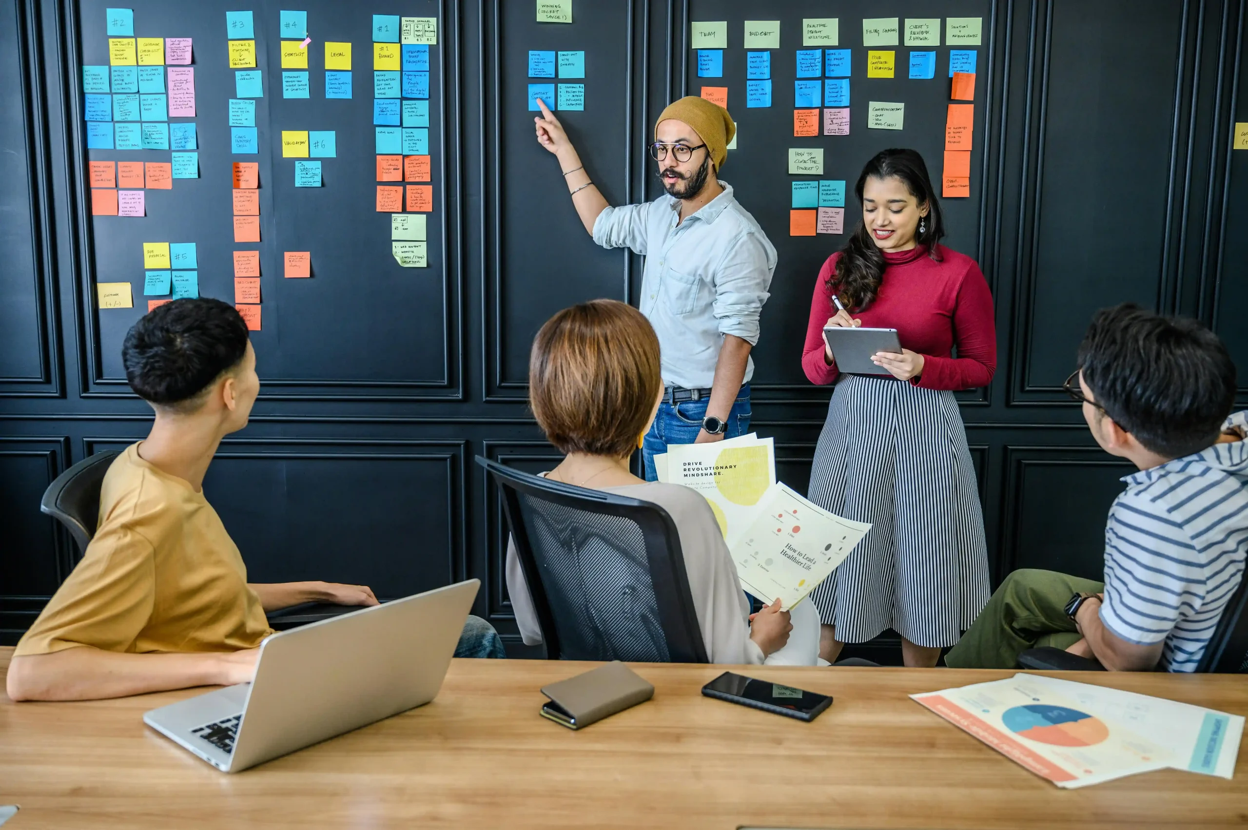 Team collaborating in a meeting room with sticky notes on a black wall, discussing project planning.