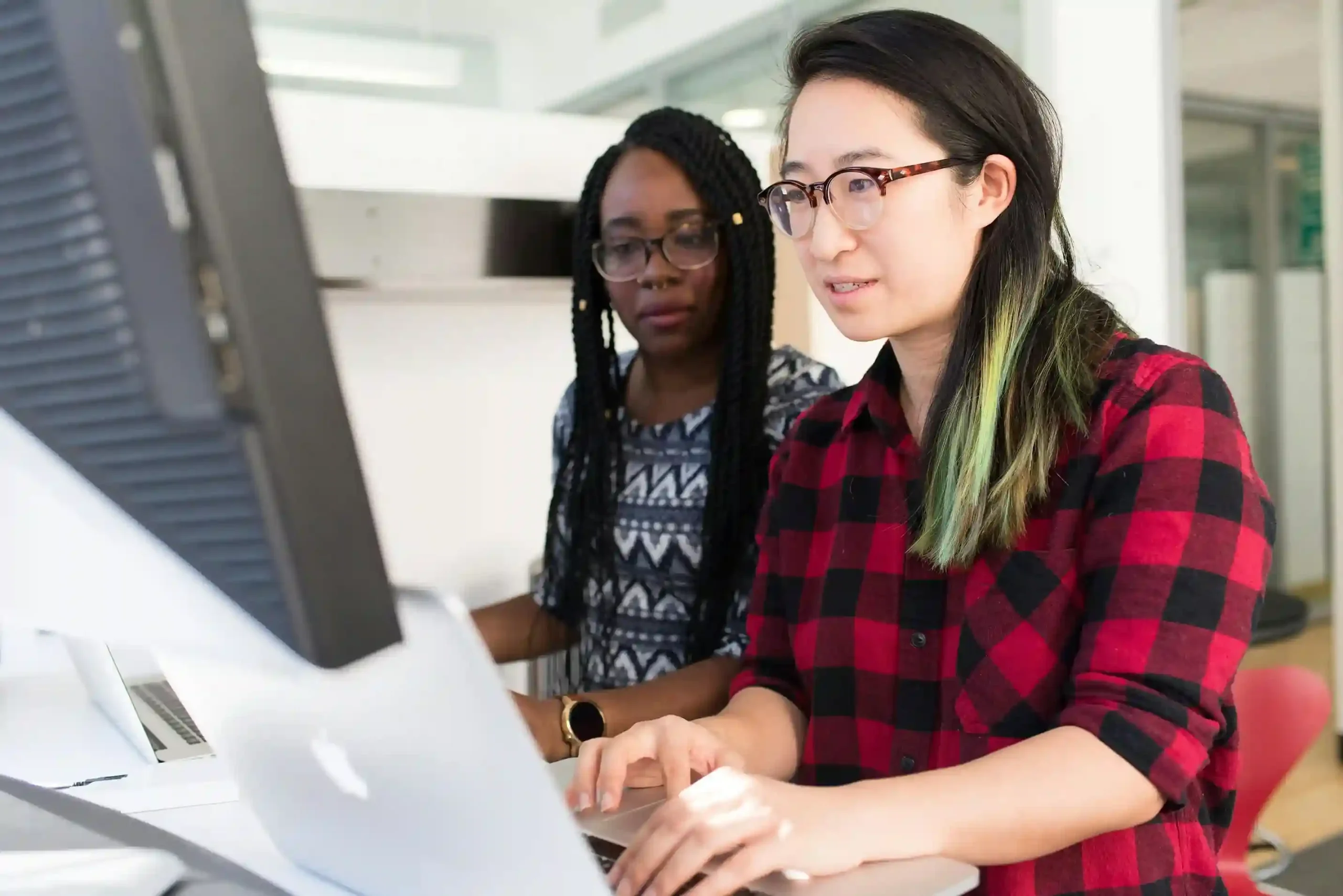 Two women collaborating at a computer in a modern office setting