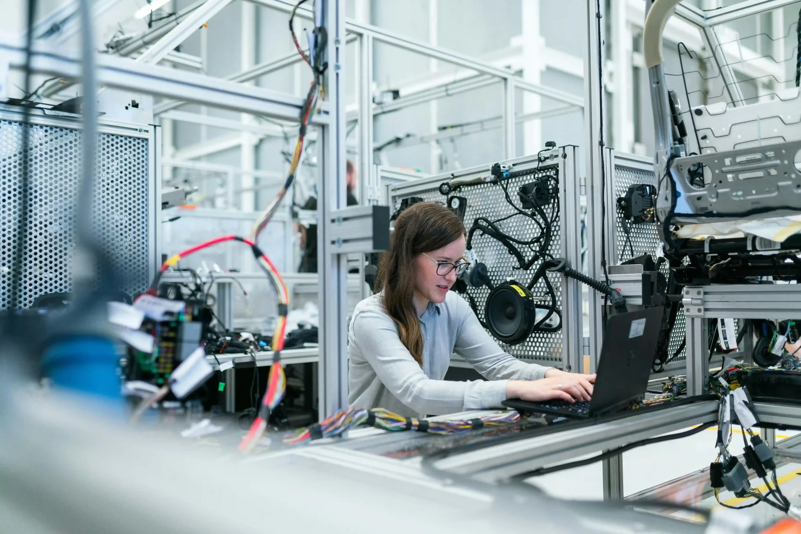 A female engineer working on a laptop in a high-tech industrial facility, surrounded by machinery and wiring.