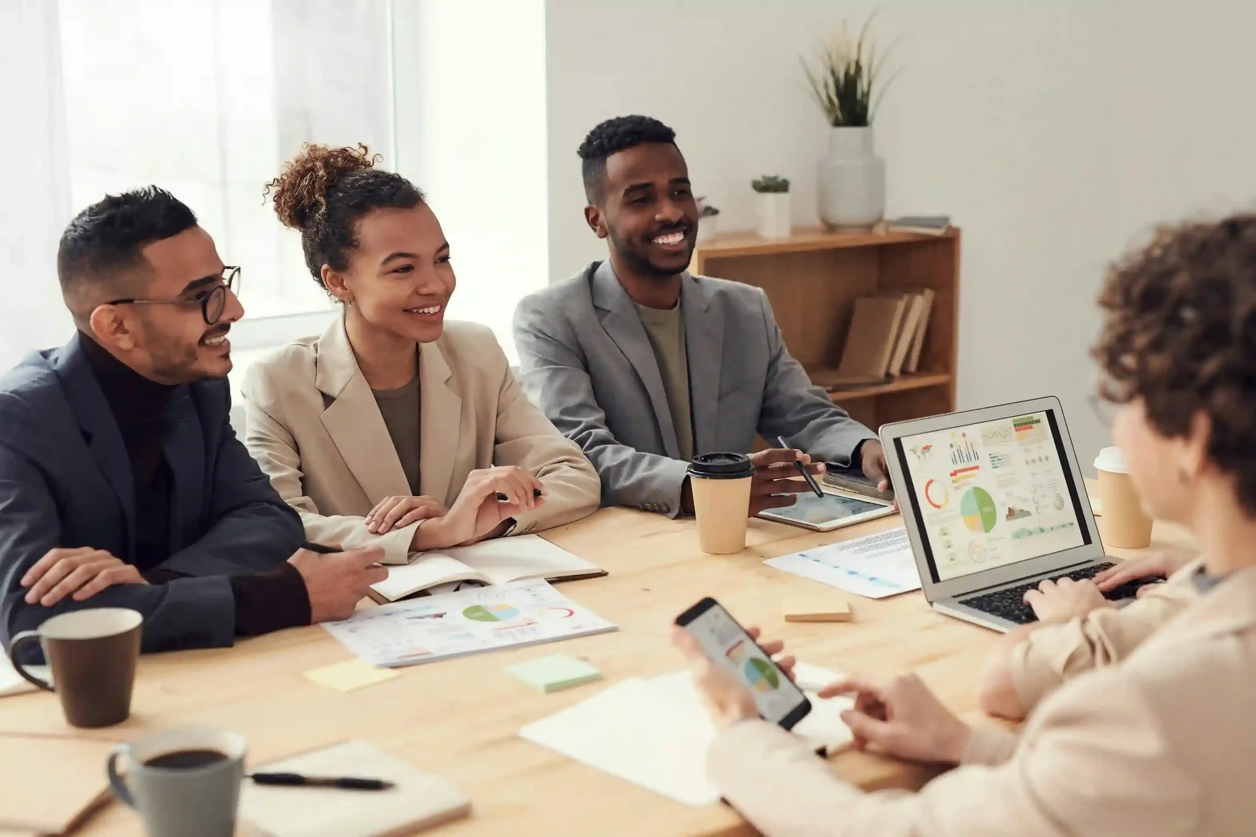 A diverse group of professionals in a business meeting, discussing data on a laptop and documents.