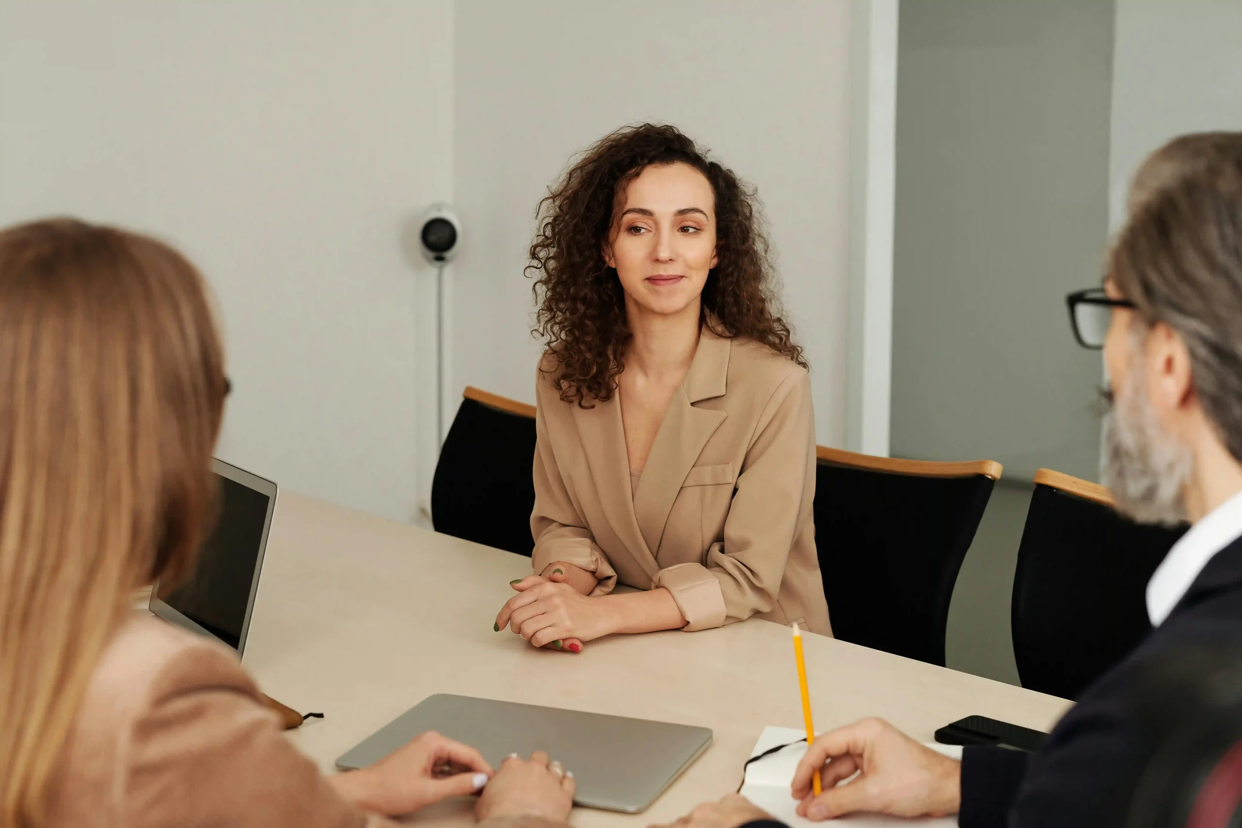 A woman in a beige blazer sits confidently at a conference table during a business meeting.
