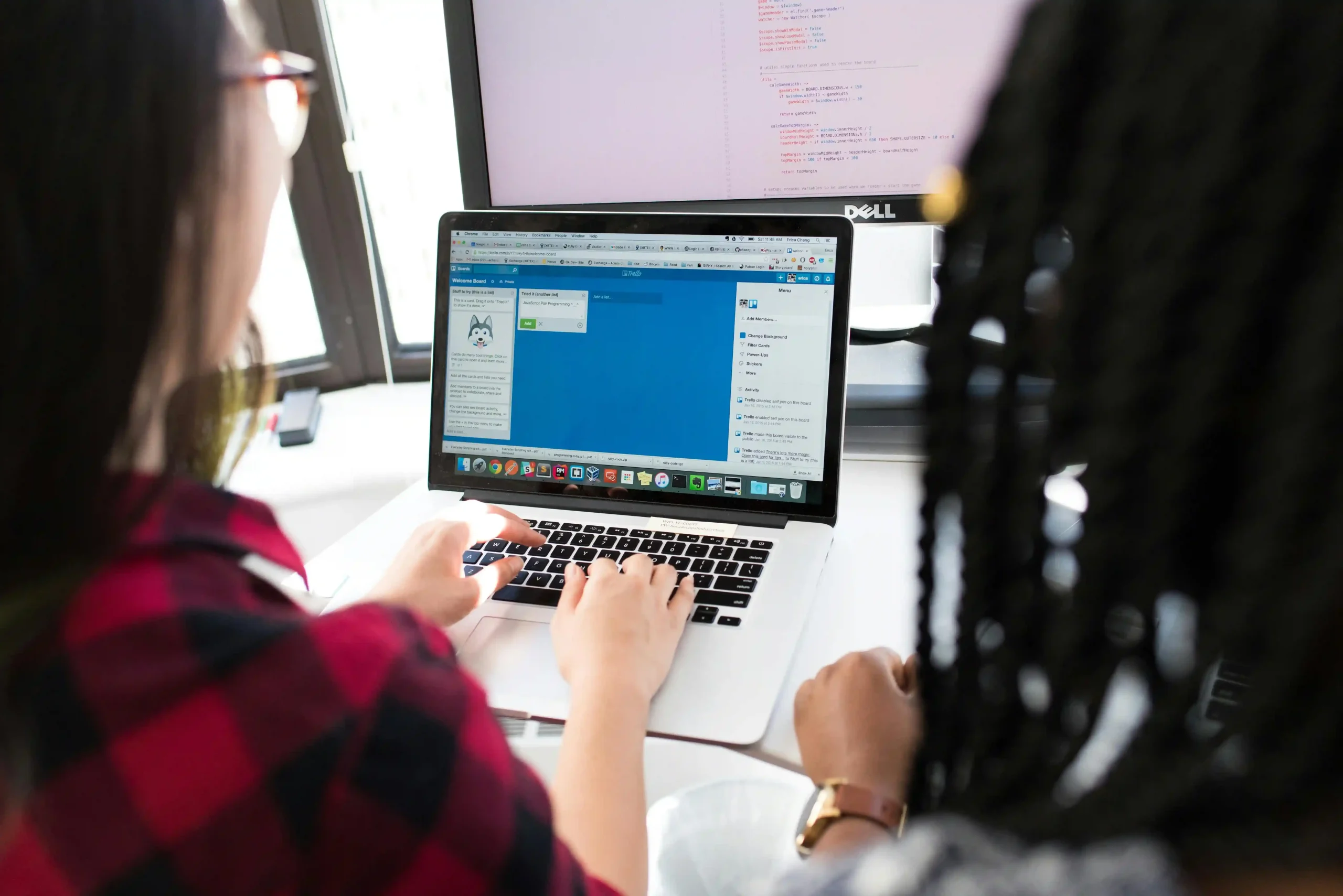 Two women working on a laptop, collaborating on a project with a task management tool open on the screen.