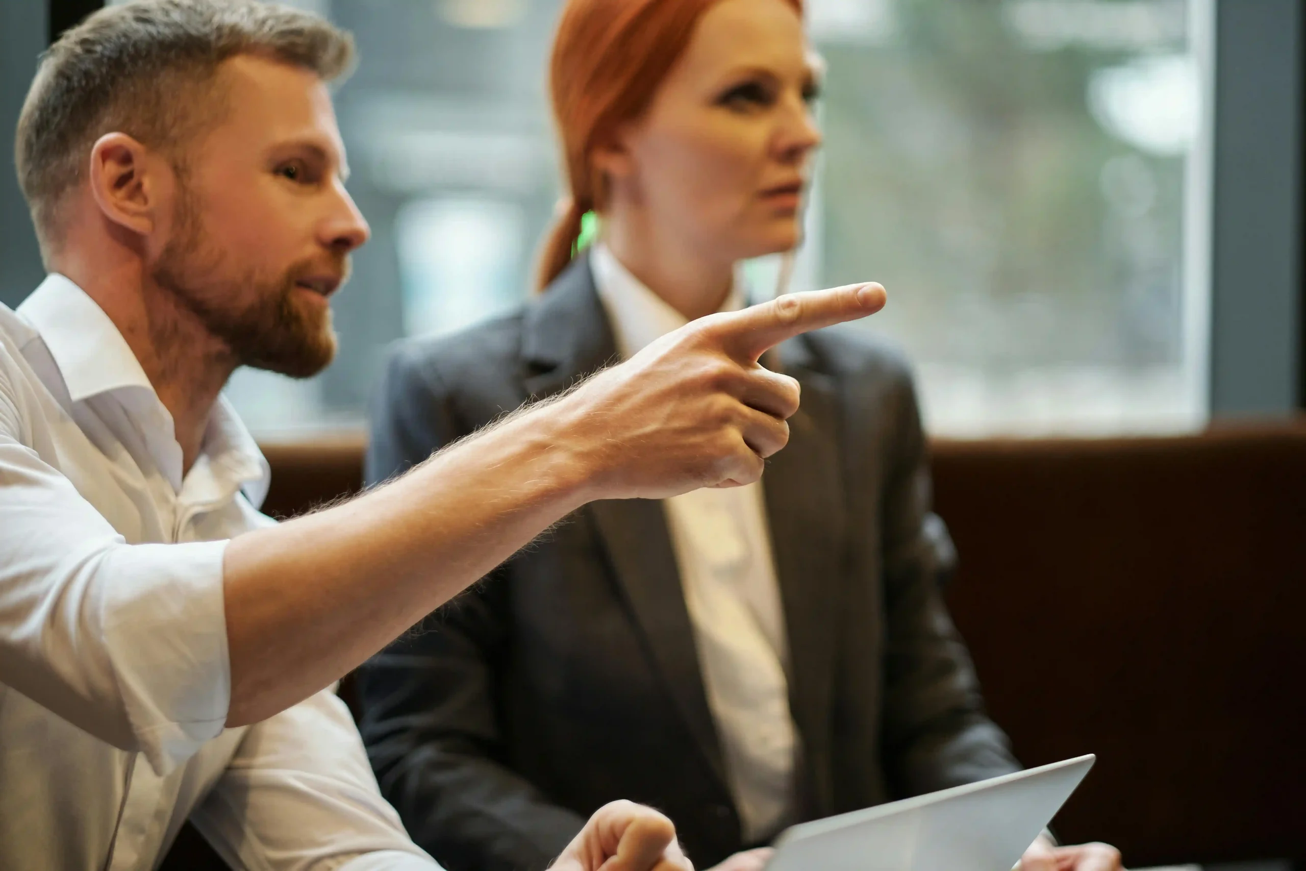 A man in a white shirt pointing while discussing with a woman in a business suit.